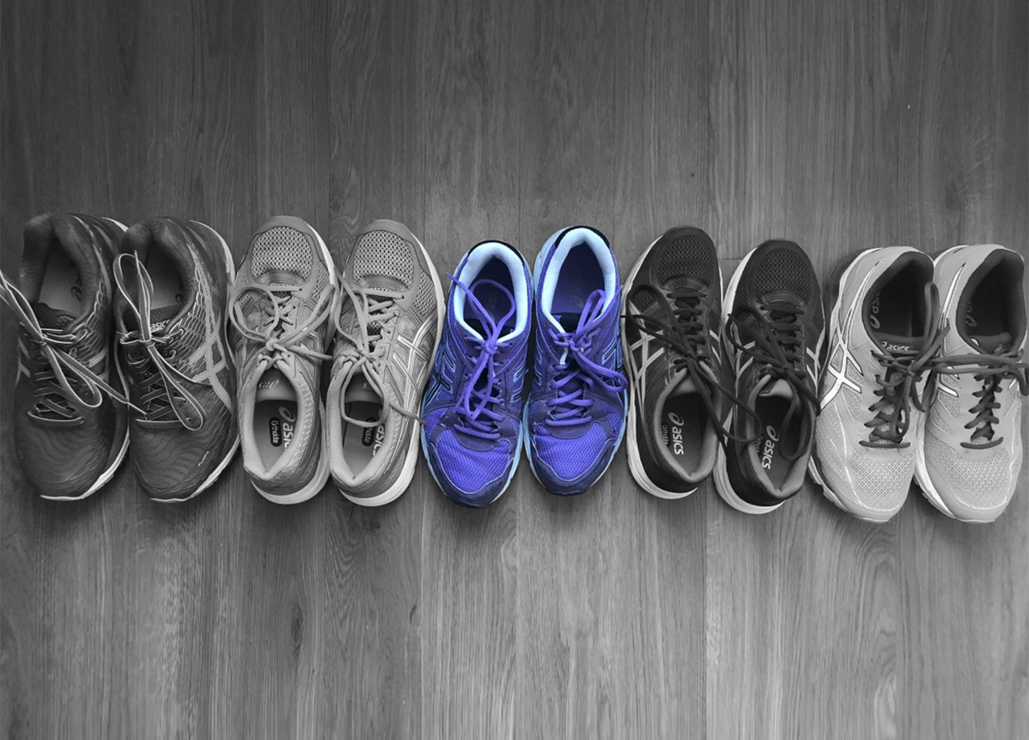 Row of running shoes on a wooden floor. The shoes are all black and white except the middle pair which are purple