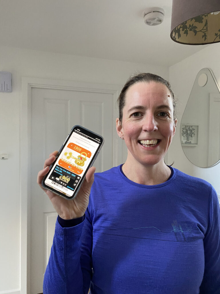 Me, certified coach and runner, wearing running gear and holding my phone which shows the results of my 2020 Run the Year Challenge
